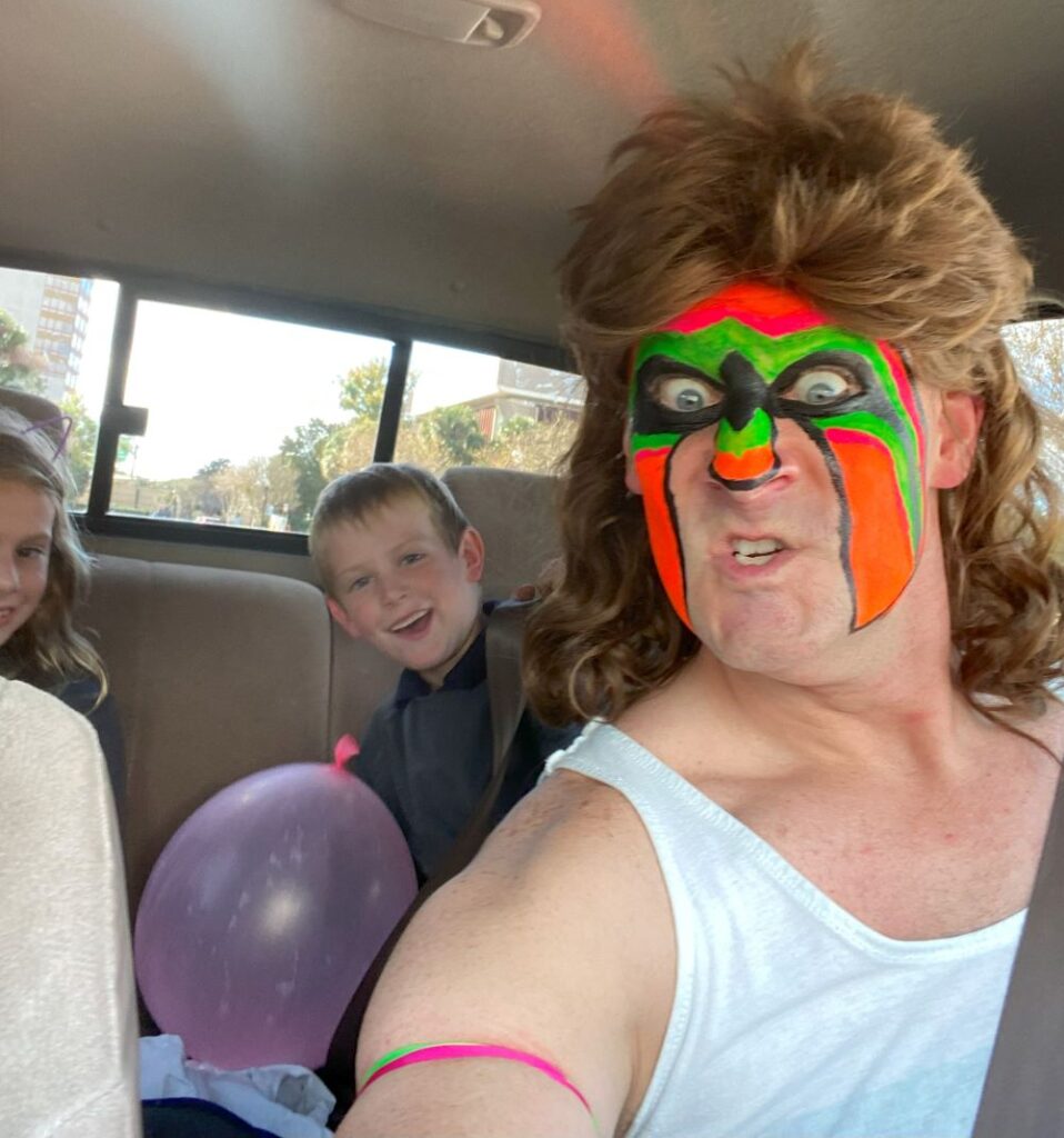 Dad in Ultimate Warrior costume picking up kids